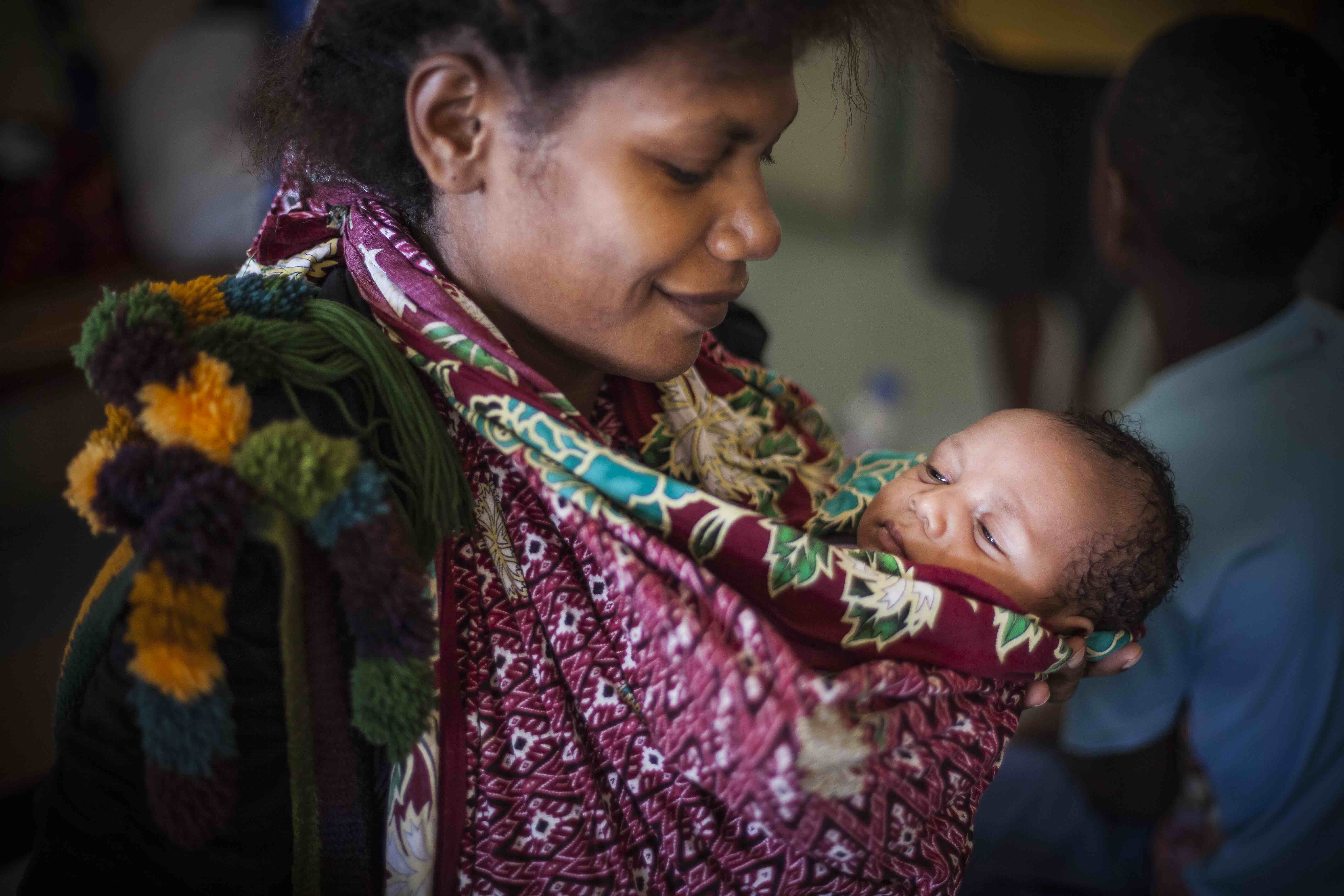 Child in traditional 'belum' string bad, held by mother, Papua New Guinea